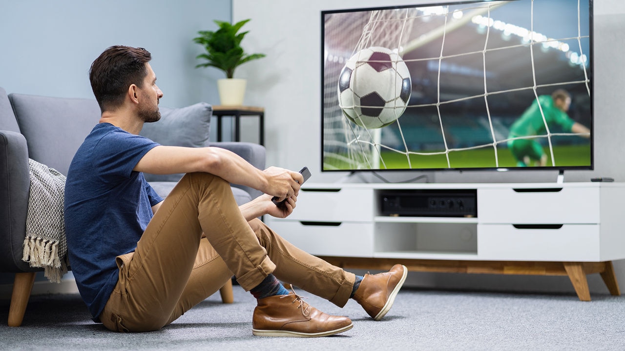 Eine Person, die ein Fußballspiel im Fernsehen schaut, verwendet einen TV Connector, um besser zu hören.