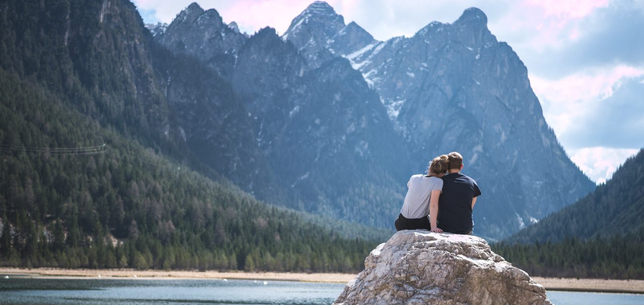 Un couple assis sur un rocher regardant un lac et les montagnes. Apprécier les sons de la nature. 